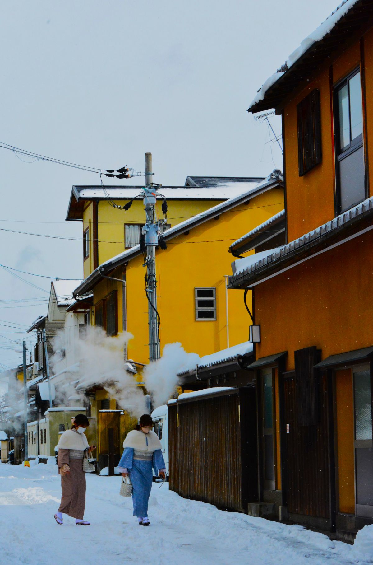 A snowy street in Nozawa Onsen with steam rising behind the houses
